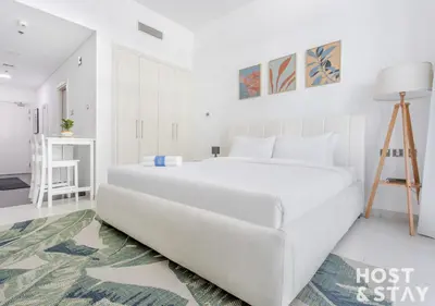 a white bedroom with a large white bed in it at Studio in Loreto 1A, DAMAC Hills - Host & Stay in Dubai