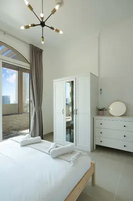 a white bedroom with a large bed and a dresser at Plaza Residences - 2BR Apartment - Allsopp&Allsopp in Dubai