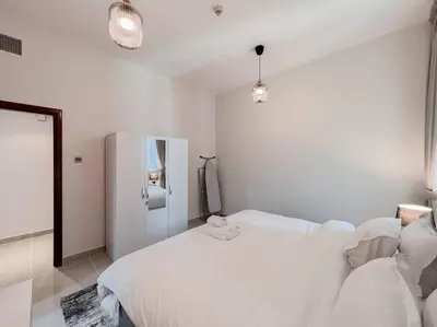 a white bedroom with a bed and a refrigerator at StoneTree - Modern 1 BR Apartment Near The Beach in Dubai