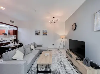 a living room with a gray couch and a tv at StoneTree - Modern 1 BR Apartment Near The Beach in Dubai