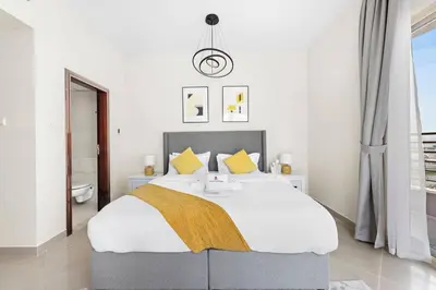 a white bedroom with a large bed with yellow pillows at StoneTree - Furnished 1BR with Modern Design in Dubai