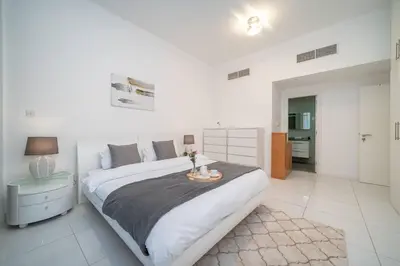 a white bedroom with a large bed with a table at StoneTree - Spacious 2BR in Great Location in Dubai