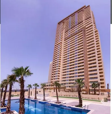 a large building with palm trees in front of a pool at Ghalia Damac Studio Apartment in Dubai