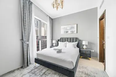 a white bedroom with a bed and a window at StoneTree - Elegant 1BR with Amazing Building Facilities in Dubai