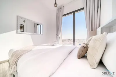 a white bedroom with a large bed with a window at Immaculate 1BR at UNA Town Square Dubailand by Deluxe Holiday Homes in Dubai