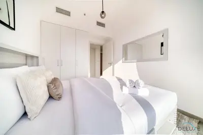 a white bedroom with two beds and a mirror at Immaculate 1BR at UNA Town Square Dubailand by Deluxe Holiday Homes in Dubai