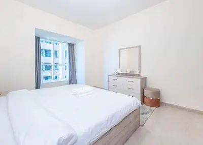 a white bedroom with a large bed and a mirror at StoneTree - Near Tram - Furnished 1BR in Dubai