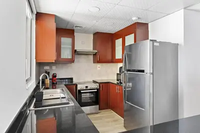 a kitchen with wooden cabinets and a stainless steel refrigerator at StoneTree - Near Beach - Furnished 1BR with Partial Sea View in Dubai