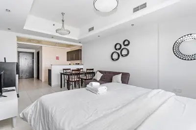 a white bedroom with a large bed and a kitchen at StoneTree - Near Metro - Furnished Studio in JLT in Dubai