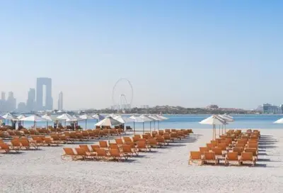 a beach with chairs and umbrellas and the ocean at StoneTree - Elegant 2BR with 1 Maids Room in Dubai