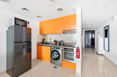 a kitchen with orange cabinets and a stainless steel refrigerator at StoneTree - Modern Stylish Studio in JLT in Dubai