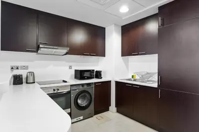 a kitchen with wooden cabinets and a washer and dryer at Nasma Luxury Stays - Elegant 1BR With Stunning View of Park Avenue in Dubai