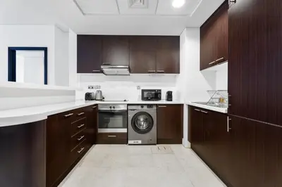 a kitchen with wooden cabinets and a washing machine at Nasma Luxury Stays - Elegant 1BR With Stunning View of Park Avenue in Dubai