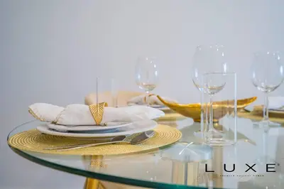 a glass table with plates and wine glasses on it at Luxe - Relax in Style Scandi 1BR with Sofa Bed in Dubai