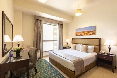 a hotel room with a bed and a desk and a window at Roda Amwaj Suites Jumeirah Beach Residence in Dubai