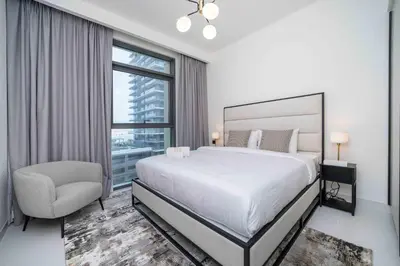 a white bedroom with a large bed and a chair at Marina Vista 1 Bed with Private Beach and Gorgeous Skyline in Dubai