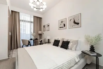 a white bedroom with a large bed and a chandelier at Modern studio in Azizi Riviera in Dubai