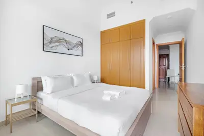 a white bedroom with a large bed and a wooden cabinet at StoneTree - Furnished 1BR with Spacious Balcony in Dubai