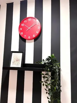 a red clock on a striped wall with a plant at Cityview Partition Room with Balcony in Tecom in Dubai