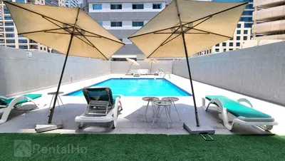 a pool with two umbrellas and chairs and a table and chairs at Luxury Studio w/ BoHo Design and Balcony for 4 Pax in Dubai