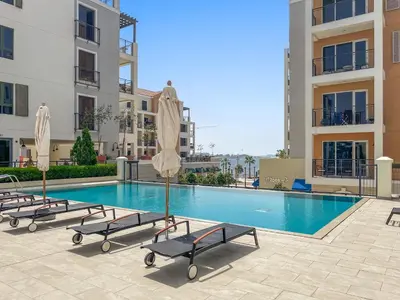 a swimming pool with chairs and umbrellas next to buildings at Spacious 1 bed in La Mer - 1 min to the beach in Dubai
