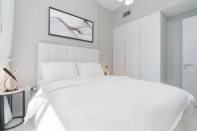 a white bedroom with a bed and a picture on the wall at Stylish Apartment in Dubai
