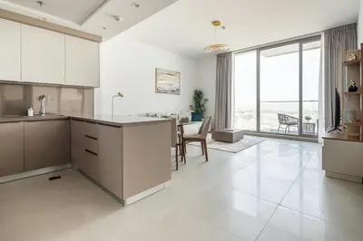 a kitchen with white cabinets and a dining room with a table at Frank Porter - Bluebell Residence in Dubai