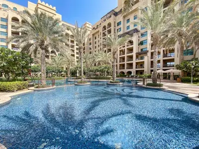 a large swimming pool with palm trees in front of a building at StoneTree - Luxurious 1BR with Beach Access in Dubai