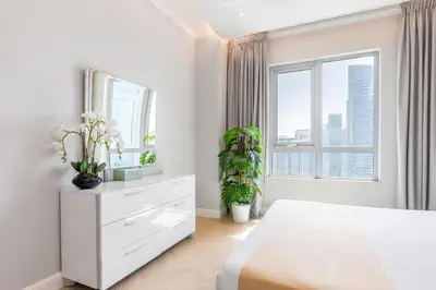 a white bedroom with a white dresser and a large window at The Residences Towers - 3 Minute Walk to Dubai Fountain in Dubai