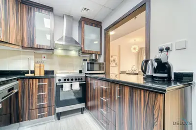 a kitchen with wooden cabinets and a black counter top at Urbane 2BR At Shams 1 JBR by Deluxe Holiday Homes in Dubai