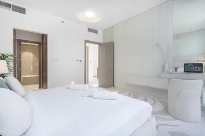 a white bedroom with a large bed and a chair at Crystal water lagoon living in District One in Dubai