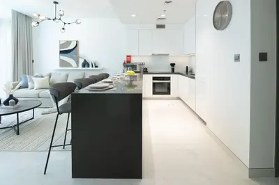 a white kitchen with a black island in a living room at HiGuests - Step Into Heaven In This Lakeside Apartment in Dubai