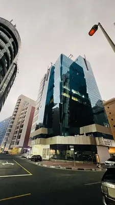 a tall glass building with cars parked in a parking lot at Dreamy Partition Room in Barsha1 in Dubai