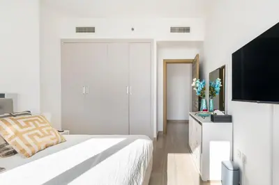 a white bedroom with a bed and a tv at Dubai Dreamland 1BR for 4, King Bed, Pool, Sauna, Gym, Free Parking in Dubai