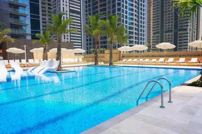 a large swimming pool with palm trees and umbrellas at 1BDR in Marina Gate Skylineview in Dubai