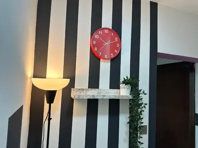 a red clock on a striped wall next to a lamp at Striped Partition Room in Barsha 1 Near Mall of the Emirates in Dubai