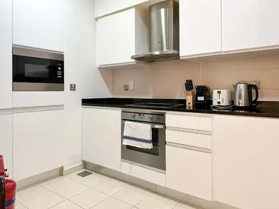 a kitchen with white cabinets and a stove top oven at Upgraded 1BR Paradise With Private Garden - Oceana in Dubai