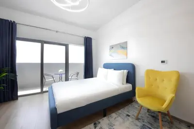 a bedroom with a bed and a yellow chair at Aura Azizi - Downtown Jabel Ali by Golden Casa in Dubai