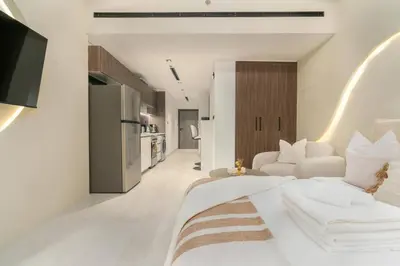 a white bedroom with a large bed and a kitchen at Unique Studio in JVC - Dubai in Dubai