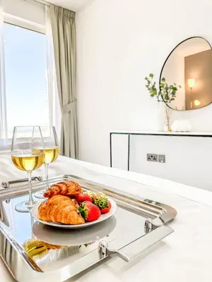 a plate of food and a glass of wine on a tray at GMA Murjan 2BR Sea View High Floor in Dubai