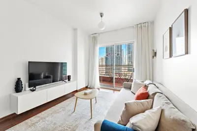 a white living room with a couch and a tv at StoneTree - Furnished 1BR in JLT with Lake View in Dubai