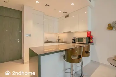 a kitchen with white cabinets and a counter with bar stools at 2ndHome - District One Residences , Residence 14 in Dubai
