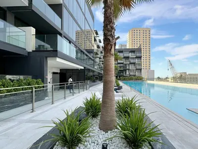 a palm tree next to a building with a swimming pool at Trophy - Stardust Sanctum Suites w Pool view in Heart of JVC in Dubai
