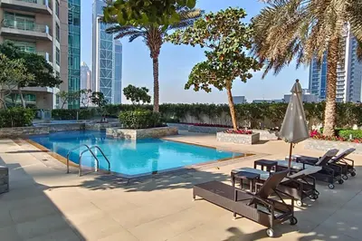 a swimming pool with chairs and an umbrella and palm trees at Close to Metro - Classic 2BR in Loft East,Downtown in Dubai