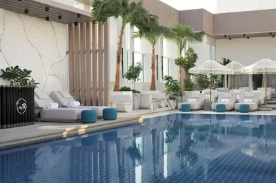 a hotel pool with white chairs and palm trees at Sheraton Grand Hotel, Dubai in Dubai
