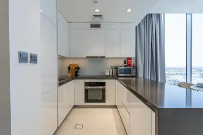 a kitchen with white cabinets and a large window at Residence 12 I District One I 1 Bedroom Apartment in Dubai