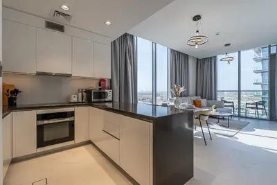 a kitchen with white cabinets and a dining room at Residence 12 I District One I 1 Bedroom Apartment in Dubai