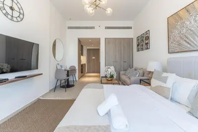 a white bedroom with a large bed and a living room at HAVN - Studio Apartment in Pantheon Elysee, JVC in Dubai