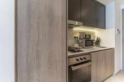 a kitchen with wooden cabinets and a stove at HAVN - Smart Home Studio in Oxford 212, JVC in Dubai