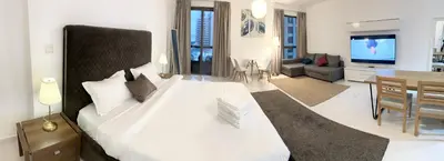 a bedroom with a large white bed and a living room at Seaside Spacious Studio with Vibrant Vibes in JBR By SWEET HOMES in Dubai